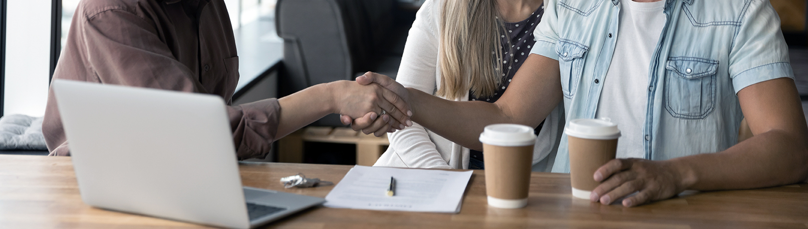 Professional skilled female financial advisor or real estate agent shaking hands with satisfied young couple clients, making agreement after negotiating contract terms at meeting in modern office.
